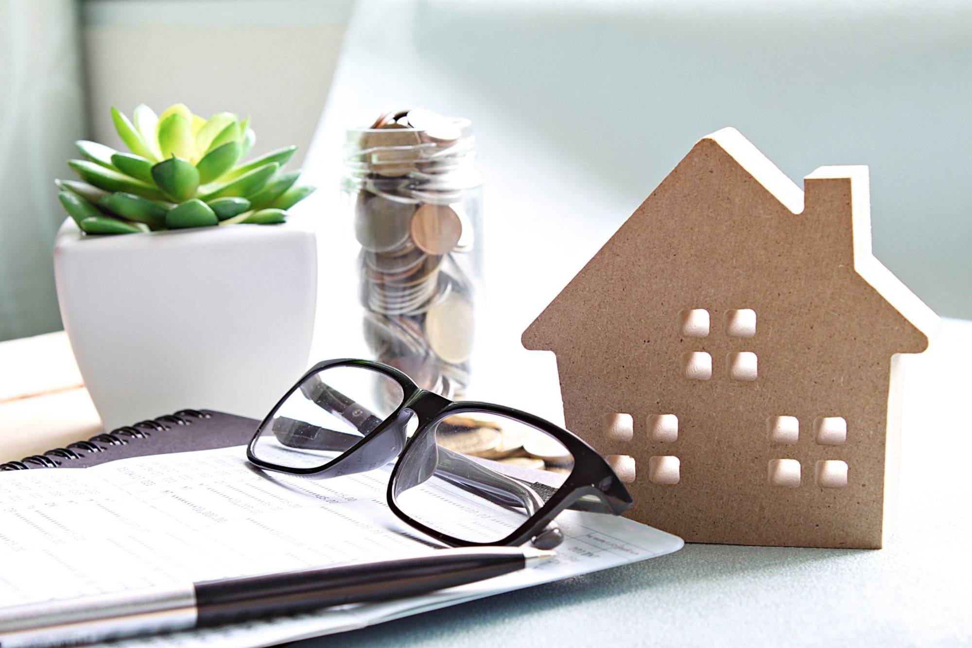 Wood house model, coins, eyeglasses and saving account book or financial statement on office desk table